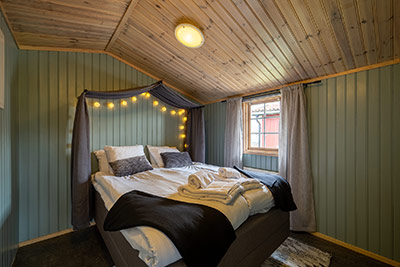 Sovrum med dubbelsäng, träpanel och ljusslinga