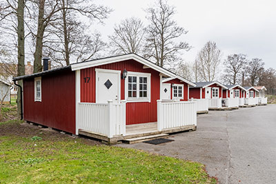 Rad av röda campingstugor med vita knutar och verandor längs asfalterad väg