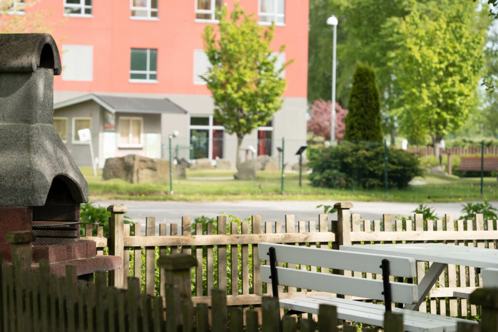 Stenugn och trästaket framför rosa flervåningshus med lekplats i bakgrunden