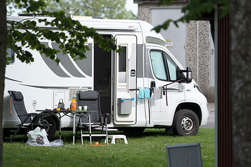 Vit husbil med utfälld markis, campingstolar och utrustning på grön campingplats