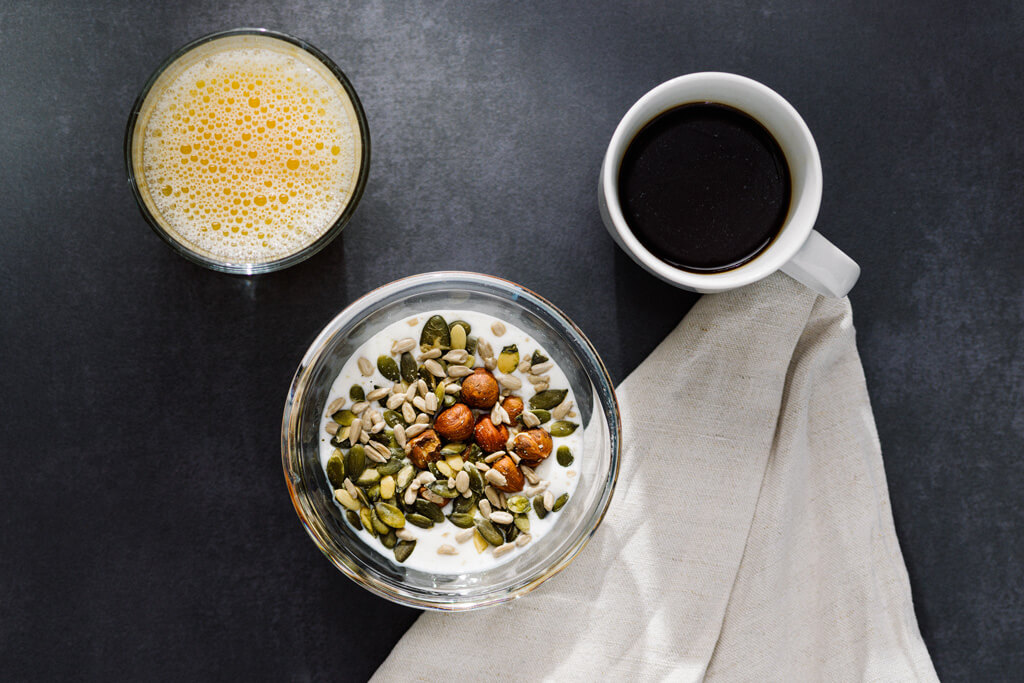 Frukost med yoghurt, nötter, frön, juice och kaffe på mörk bricka