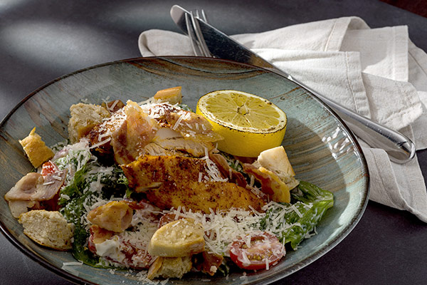 Caesarsallad med grillad kyckling, citron, krutonger och parmesan på grön tallrik