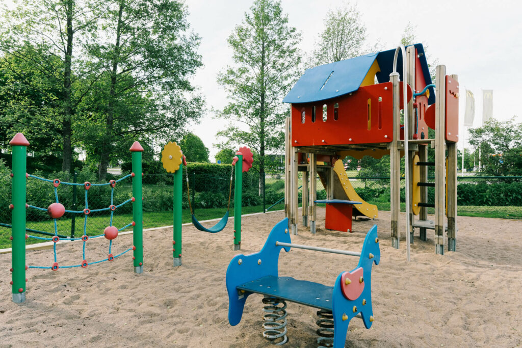 Lekplats med klätternät, gungdjur och lektorn med rutschkana i parkliknande miljö