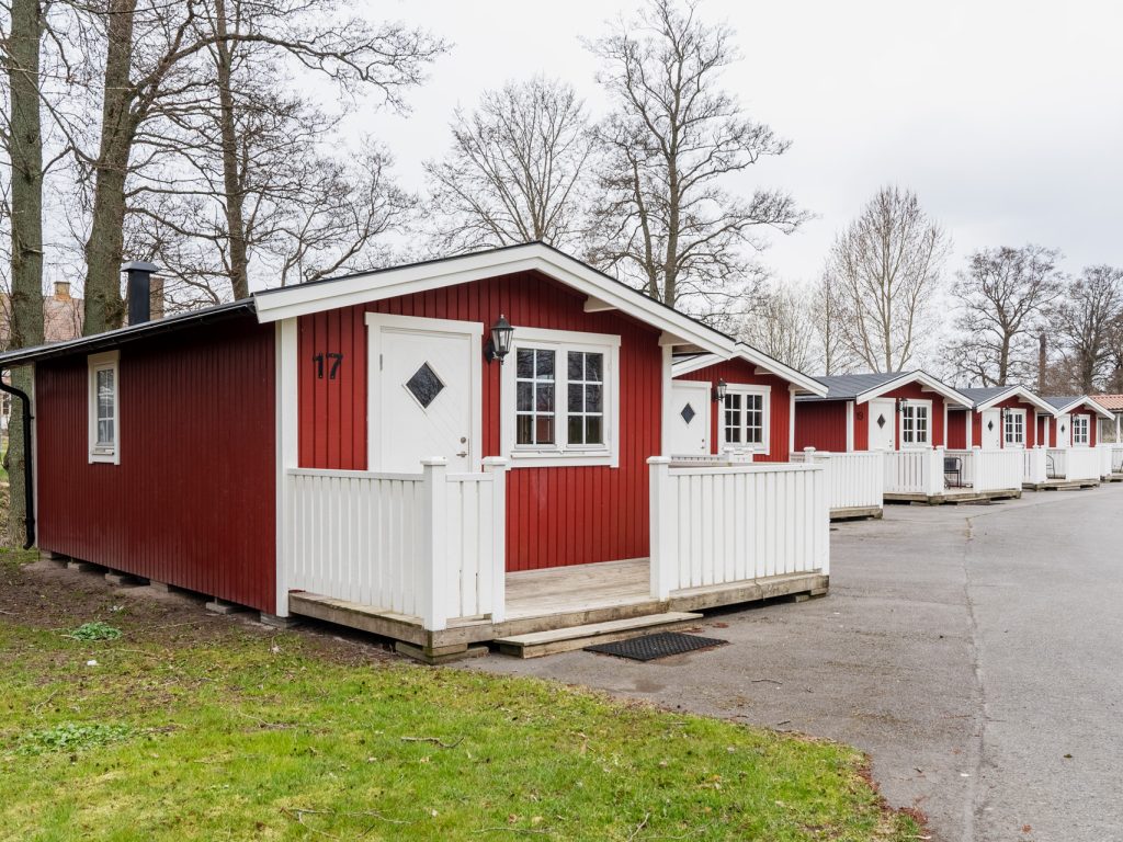 Rad av röda campingstugor med vita knutar och verandor längs asfalterad väg